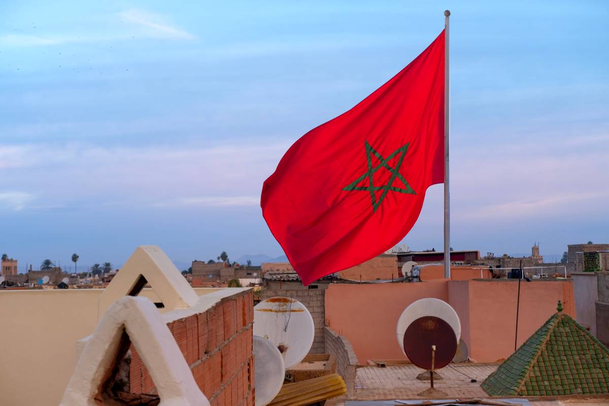Drapeau marocain flottant sur un toit à l'aube dans un quartier résidentiel, symbolisant la nationalité marocaine.