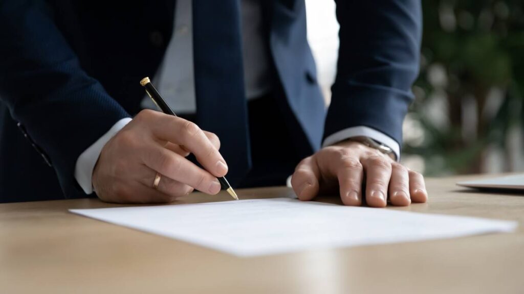 Un homme en costume signe un document pour la légalisation de sa signature.